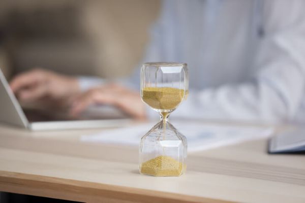 hourglass on a desk in front of a professional's hands typing on a computer